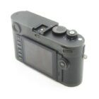 A rear view of a black digital camera showing its LCD screen and various control buttons, including a mode dial on top.