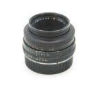 A black camera lens with multiple engraved markings, including "SUMMICRON-R 1:2/50," featuring an aperture and focus ring, set against a plain white background.