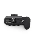Bottom view of a Leica digital camera, displaying various labels and markings, including the model number and manufacturer details, with a circular lens mount and battery compartment cover visible.