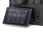 Close-up of a digital camera's rear tilt-out screen displaying various settings such as aperture, shutter speed, ISO, and exposure value, with nearby buttons labeled PLAY, FN, and MENU.