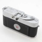 A vintage Leica camera with a silver top and black body featuring a textured grip and dials on the top panel.