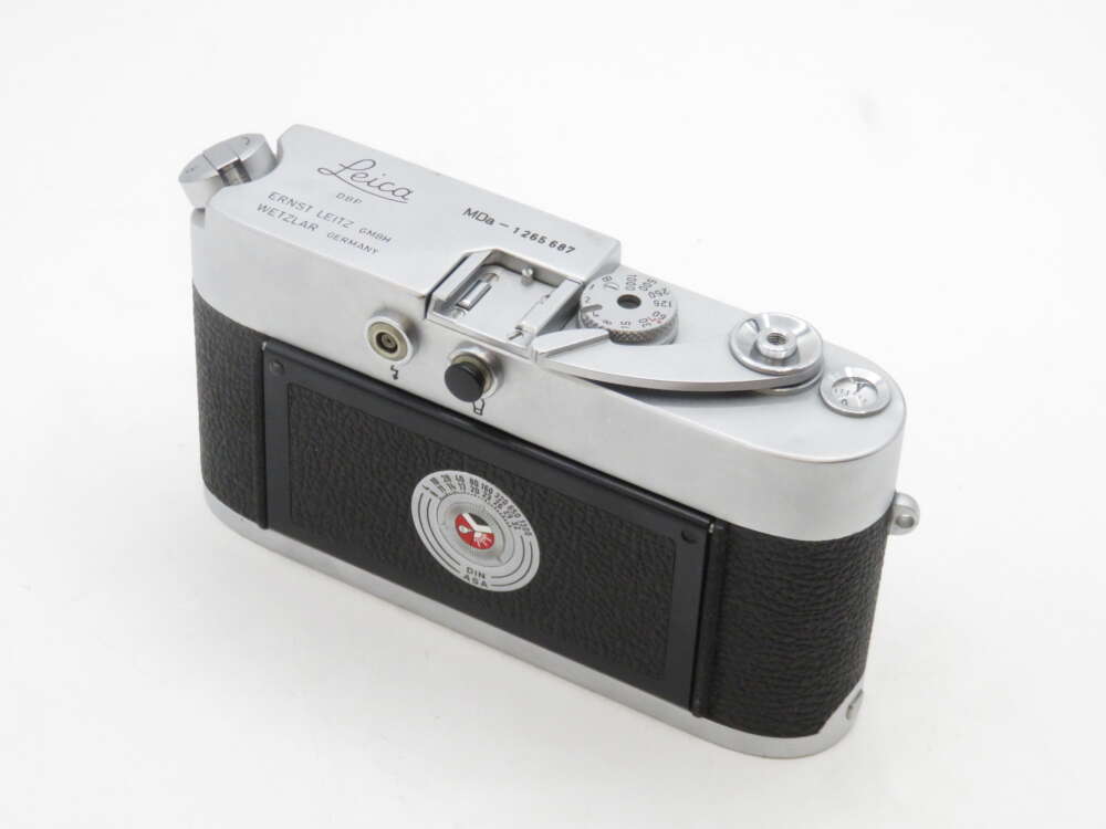 A vintage Leica camera with a silver top and black body featuring a textured grip and dials on the top panel.