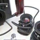 Close-up view of multiple camera lenses equipped with handles and metal supports, placed on a white surface, including a lens marked with '150mm' and a wooden grip visible in the background.