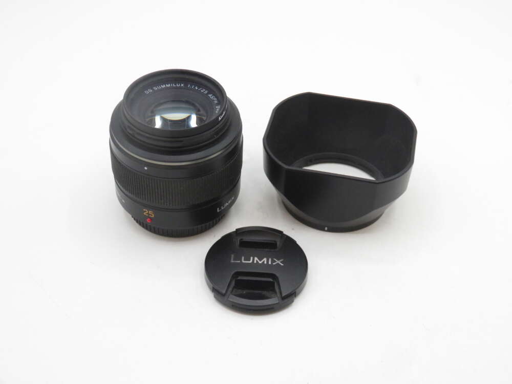 IMG_2093 A Lumix 25mm camera lens with its lens hood and cap placed on a white surface.