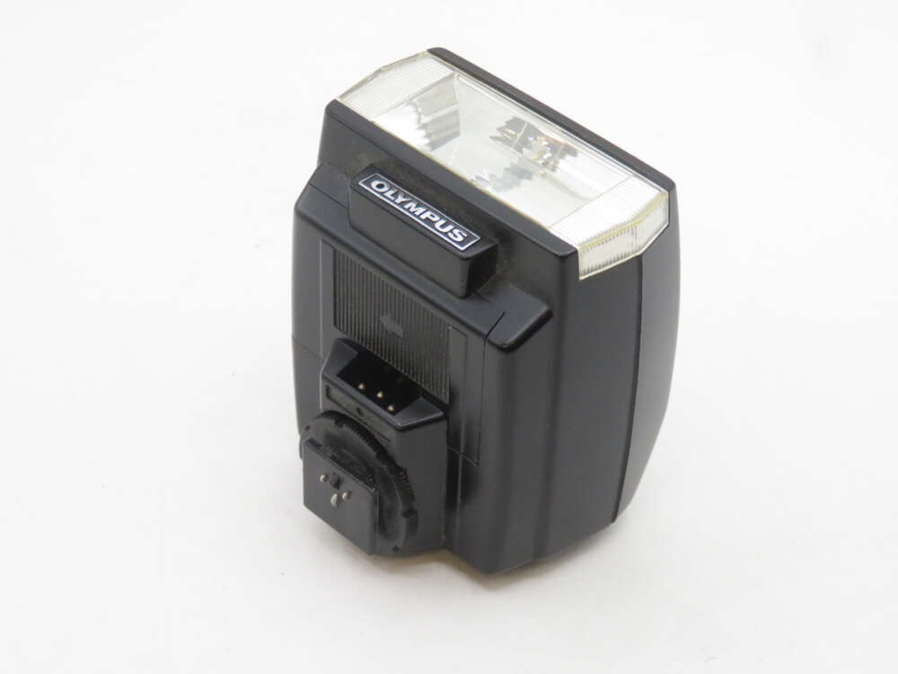 IMG_2136 A black Olympus camera flash unit with a transparent front cover and a branded label on top, shown against a plain white background.