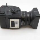 A medium format camera with a large lens and square lens hood, viewed from the side against a white background.