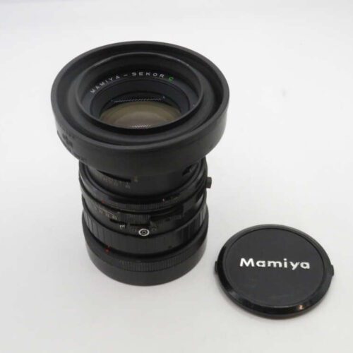 A Mamiya-Sekor camera lens with several adjustment rings, placed next to a black lens cap with 'Mamiya' printed on it, on a white surface.