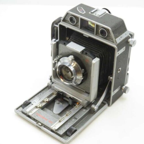 A vintage folding camera with bellows, metal body, and viewfinder, placed on a white surface.