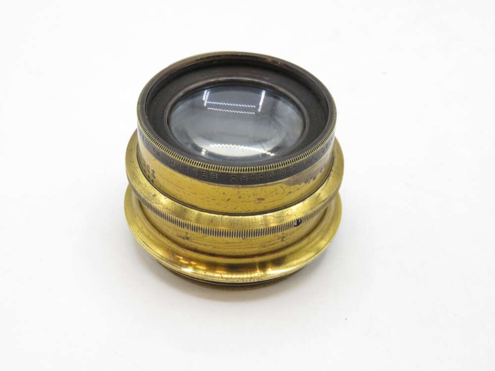 IMG_2228 A vintage brass camera lens with engraved markings, displayed against a plain white background.