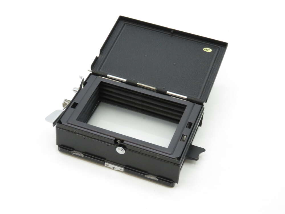 IMG_2253 A black photographic film holder with an open top, showing its internal compartment and metal clasps on the sides.