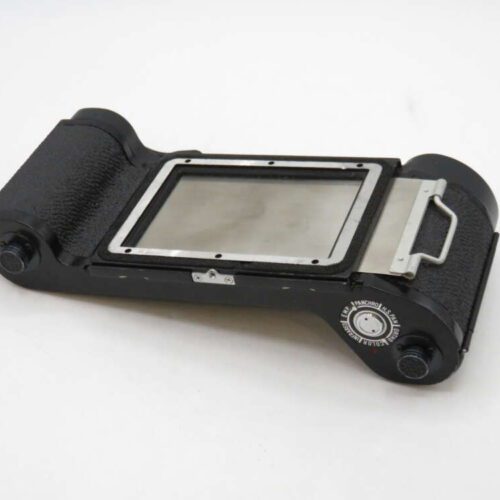 A vintage black film back accessory with a rectangular opening and metal details, used for medium format cameras.