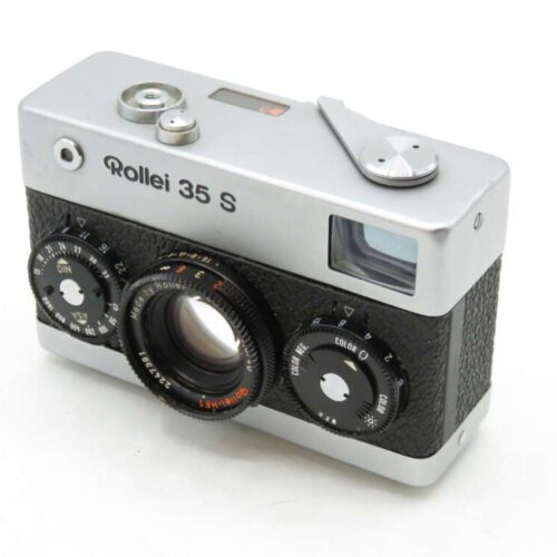 A vintage Rollei 35 S film camera with a compact design, featuring a silver top and bottom with black textured grip. It has a lens marked with 'Made in Germany,' and various settings dials are visible on the front.