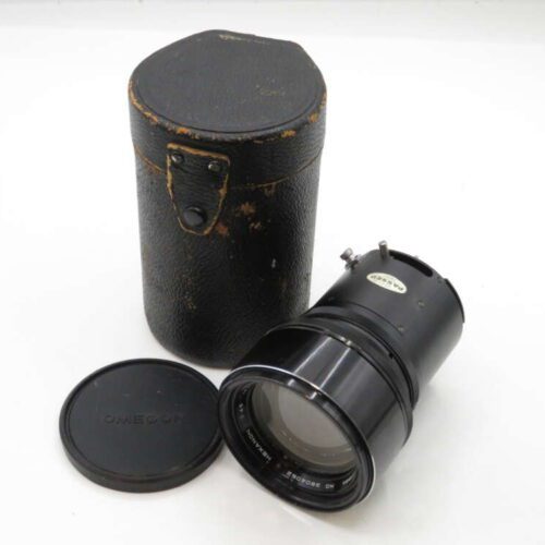 A vintage camera lens with a black metal body, accompanied by a protective carrying case and a lens cap with the logo 'OMEGON'.