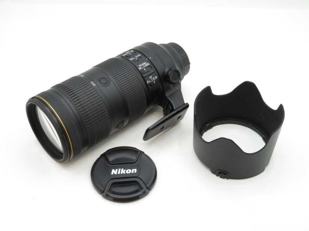 IMG_2273 Nikon camera lens with an attached tripod collar, a detached lens hood, and a lens cap displaying the Nikon logo.