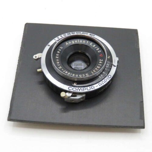 A vintage camera lens labeled "Angulon 1:6.8/90 Schneider-Kreuznach" mounted on a black square base, with Compur-Rapid shutter controls visible.