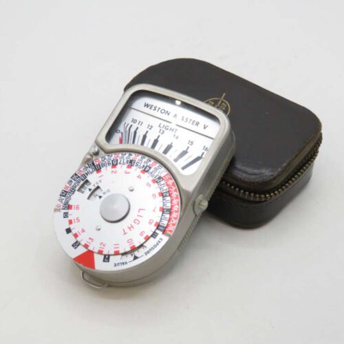 A vintage Weston Master V light meter with a circular dial, placed on a small brown zippered case.