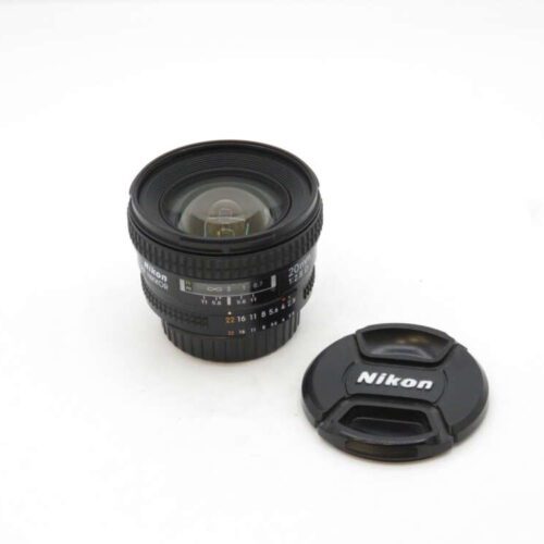 A Nikon NIKKOR 20mm f/2.8D wide-angle lens with the lens cap placed beside it on a plain white surface.
