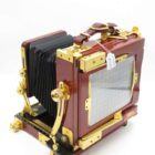 A vintage wooden large format camera with brass fittings and black bellows, showcasing intricate details and craftsmanship on a plain white background.