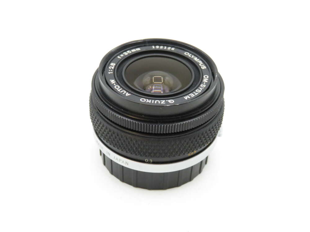 IMG_2345 A black Olympus camera lens with "OM-SYSTEM G.ZUIKO AUTO-W" and "1:2.8 f=28mm" markings, showing its aperture and focal length details.
