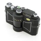A vintage Widelux camera with a black body and silver dials, showcasing a distinctive rounded lens design.