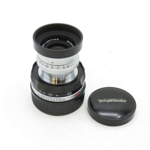 A Voigtländer camera lens with a wide aperture and an accompanying lens cap on a white background.