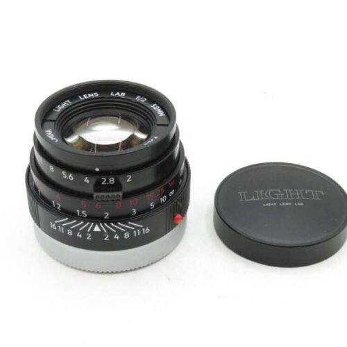 A camera lens with a silver and black design, marked "Light Lens Lab 50mm," beside a matching lens cap.