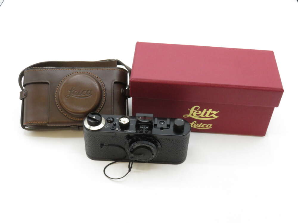 IMG_3148 A vintage Leica camera with a leather case and a red Leitz-branded box on a white surface.