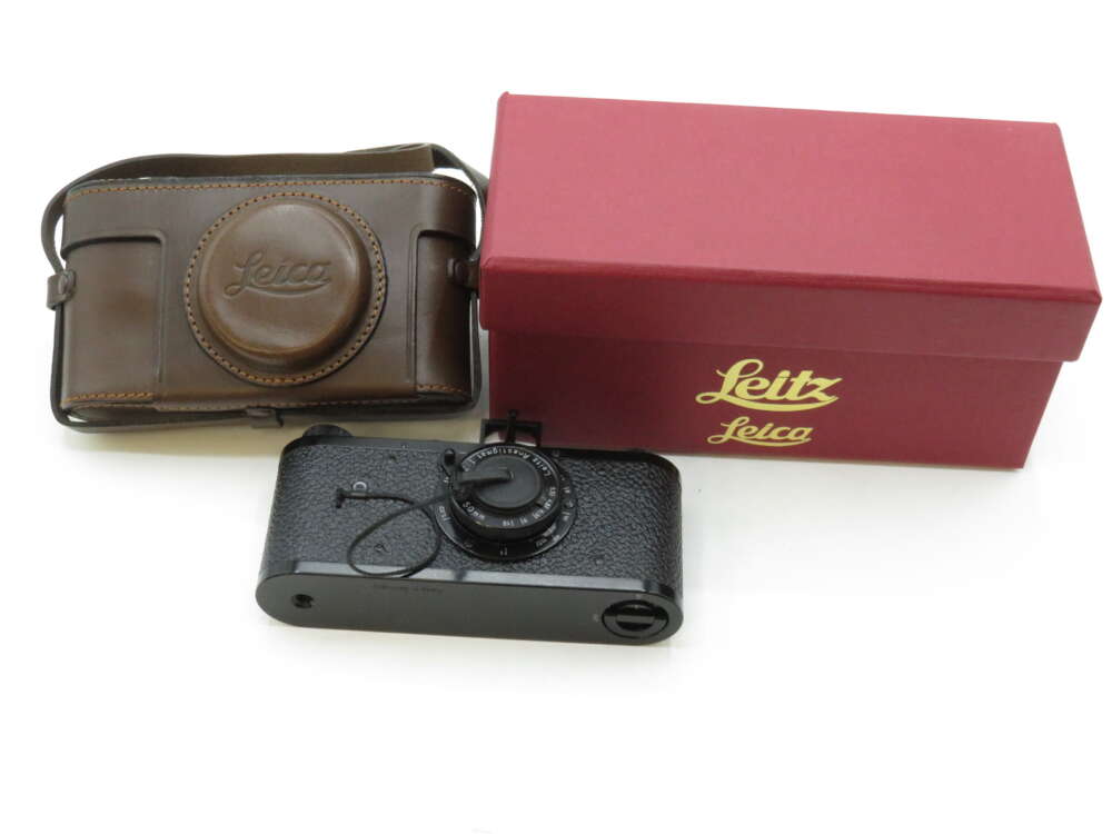 A black vintage Leica camera with a brown leather case and a red box with gold lettering.