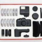 A vintage Pentax camera with accessories including lenses, a flash, filters, and carrying cases, neatly organised in a display box.
