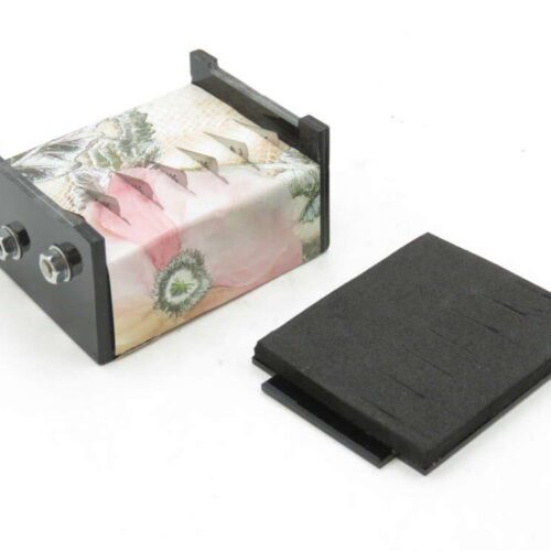 A decorative tissue holder with floral design next to a black foam pad.
