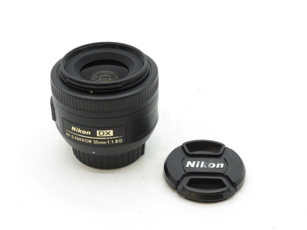 A Nikon DX AF-S Nikkor 35mm f/1.8G lens next to its detachable lens cap.