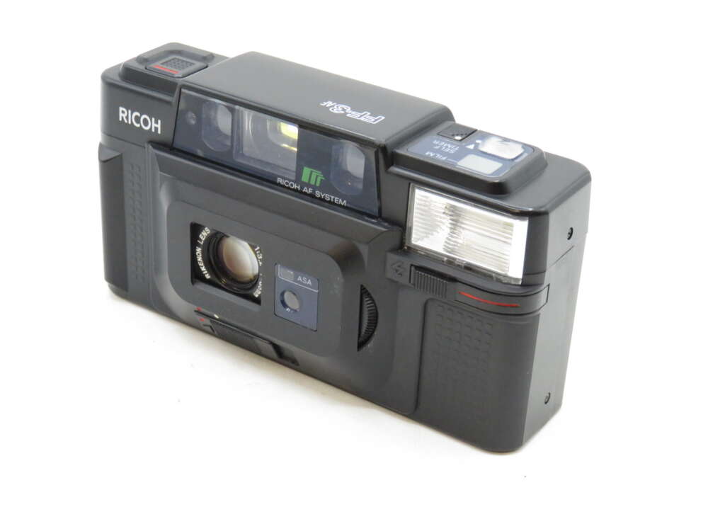 IMG_3234 Black Ricoh film camera with a lens cover, visible flash, and branding on the top left.