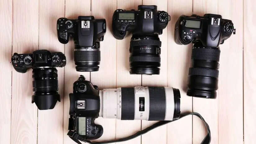 Five DSLR cameras with various lenses are arranged on a wooden surface, showcasing different camera models and lens sizes.