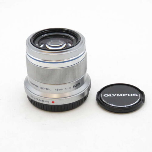 A silver Olympus 45mm f/1.8 camera lens with its cap resting on the surface beside it.