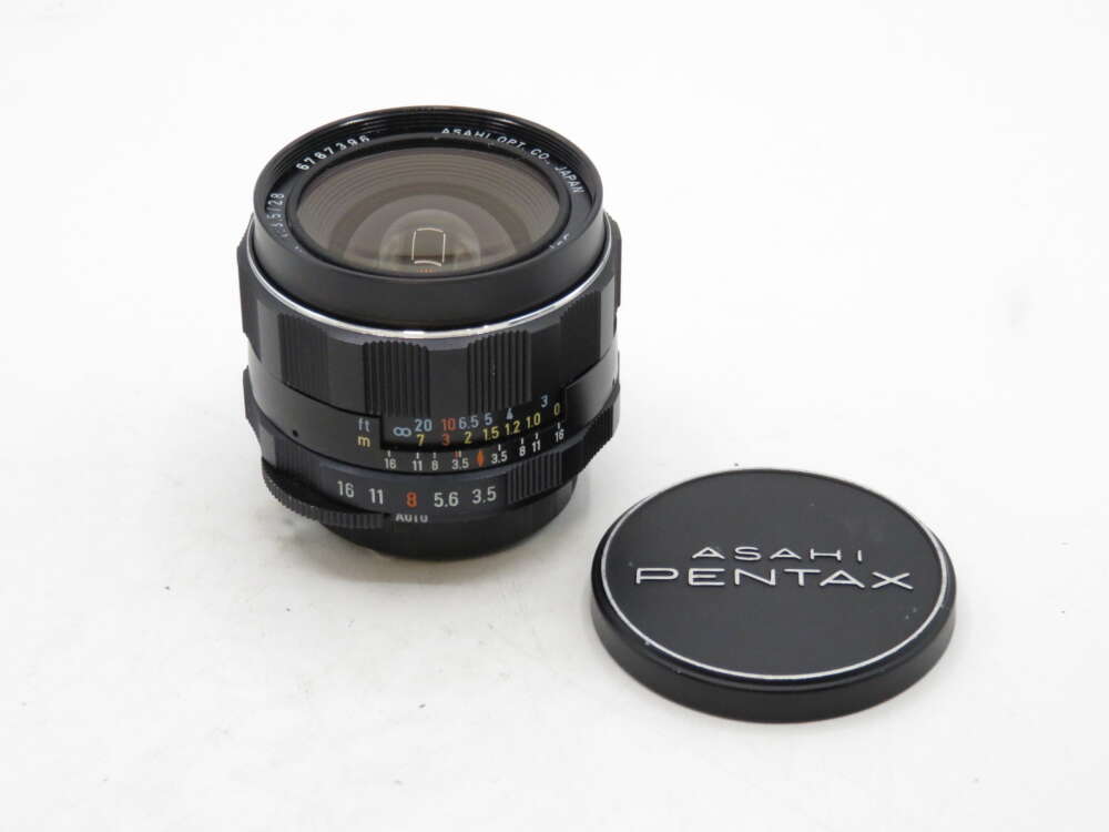 IMG_3422 A Pentax camera lens with various focus markings, alongside its lens cap on a white surface.