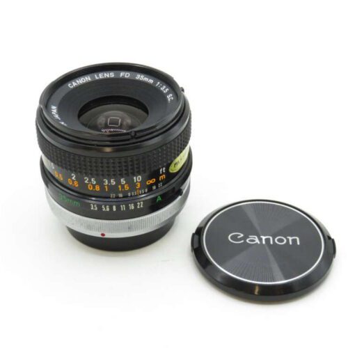 A Canon FD 35mm F/2.8 lens with detailed focus and aperture markings, next to its lens cap.