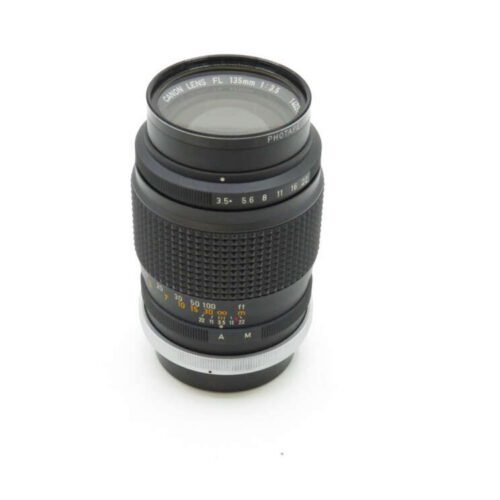 A Canon telephoto lens with a metallic focus ring and aperture markings, standing upright on a white background.