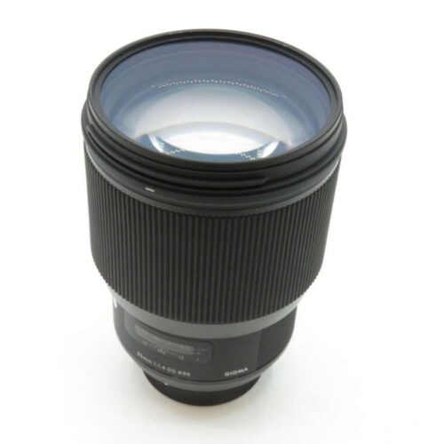 A black Sigma camera lens with a ribbed focus ring and glass elements visible at the front.