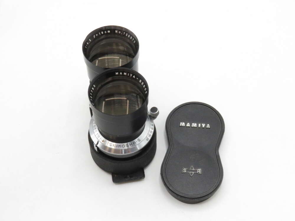 IMG_3496 Dual-lens Mamiya camera lens set with a lens cap beside it on a white background.