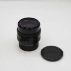 A Leica camera lens with its cap placed beside it on a plain white surface.