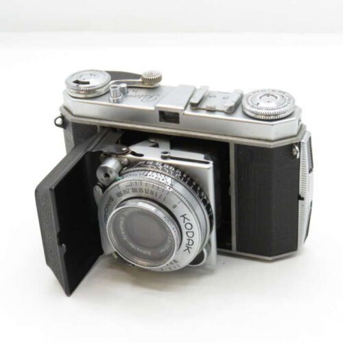 A vintage Kodak folding camera with a black bellows and silver lens housed in a partially open casing.