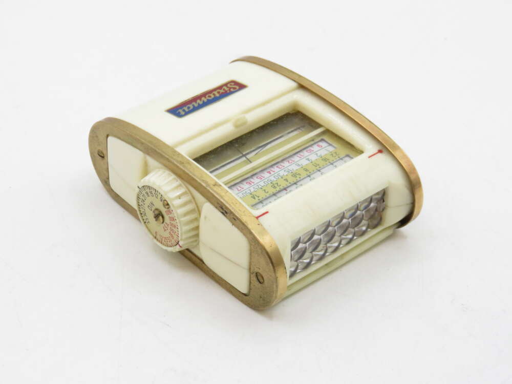 IMG_3548 A vintage mechanical manual calculator with a brass frame, a white body, and a rotating dial featuring numbers and a ruler scale.