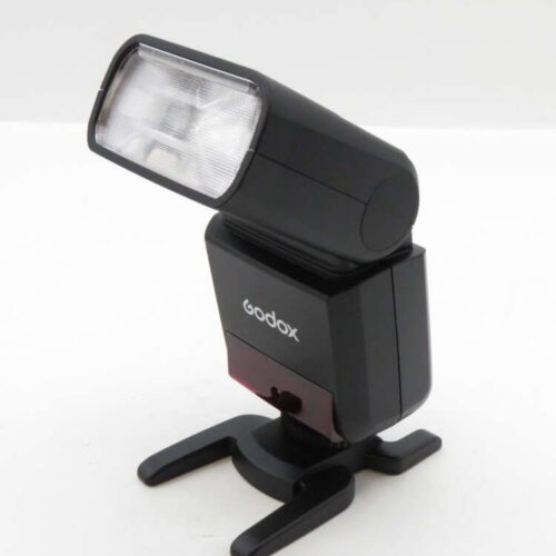A Godox camera flash with a swiveling head on a small stand, set against a plain background.