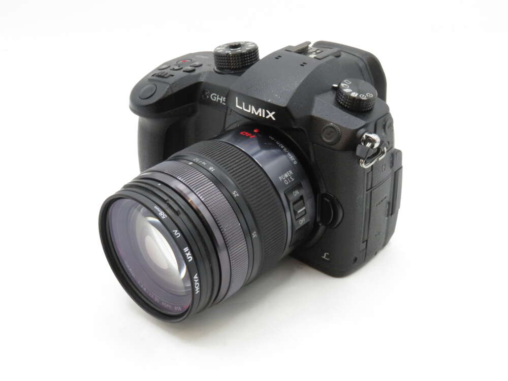 IMG_3585 A black Lumix GH5 camera with a lens attached, featuring various buttons and dials on the top.