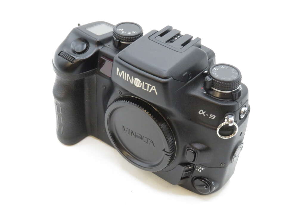 IMG_3598 A Minolta α-9 SLR camera with a prominent grip, numerous control dials, and the lens cap attached.