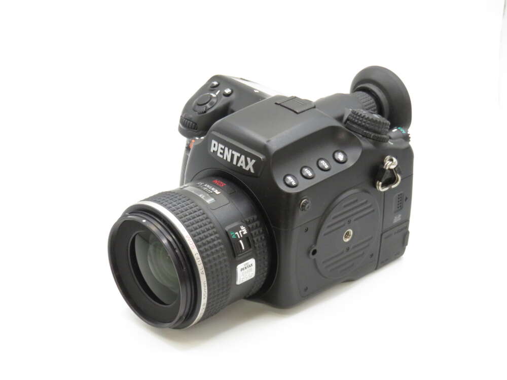 IMG_3604 A black Pentax DSLR camera with a zoom lens, numerous buttons, and a viewfinder on a white background.