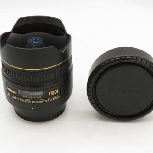 A Nikon Fisheye NIKKOR 10.5mm lens with its cover beside it on a white background.