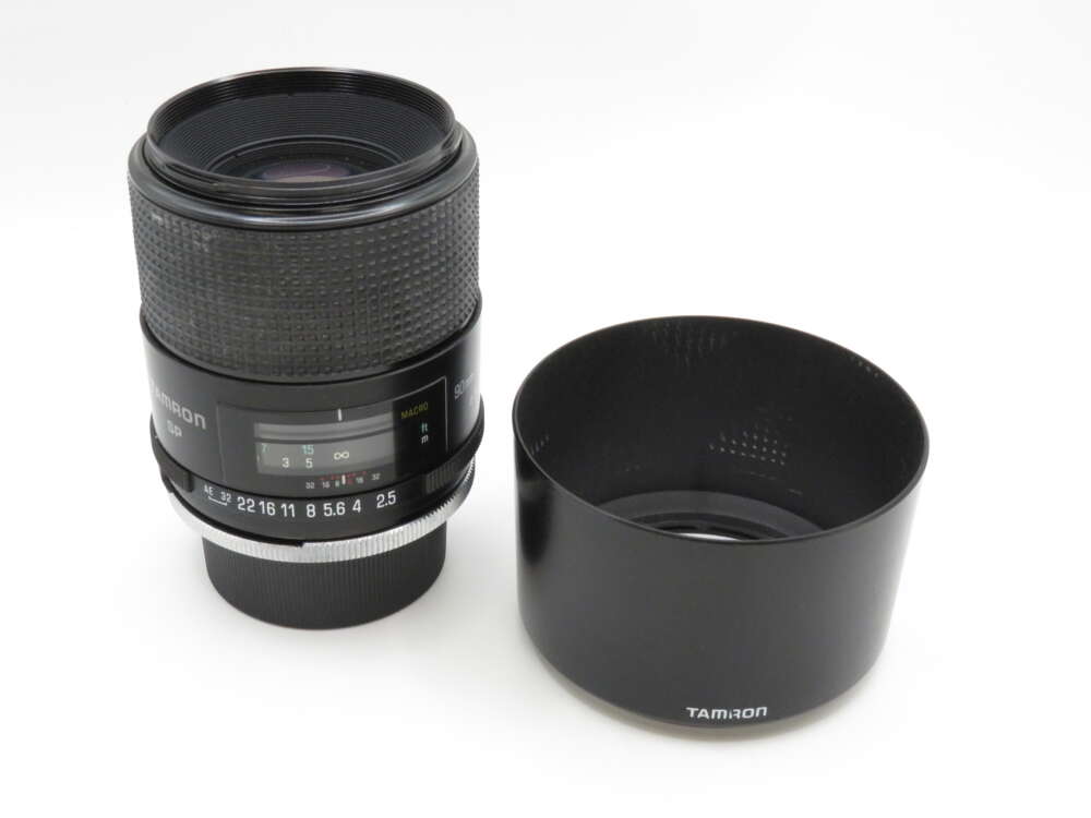 IMG_3674 Tamron camera lens with hood placed beside it on a white surface.