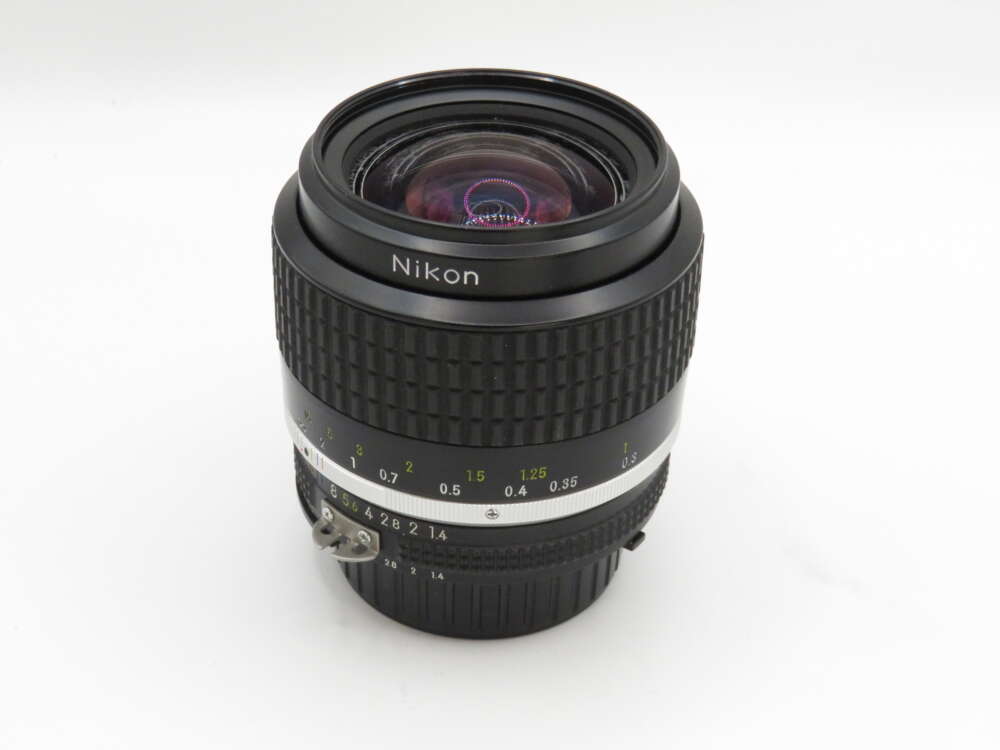 IMG_3694 Nikon camera lens with a black body, focus rings, and distance markings, positioned against a plain white background.