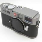 A silver and black Leica M9 camera featuring a prominent lens mount cap and various control dials on top.